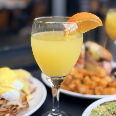 Mimosa cocktail featuring orange wedge garnish, served in a wine glass.
