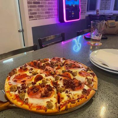 Whole pizza topped with pepperoni, sausage, and bacon, served on the table.