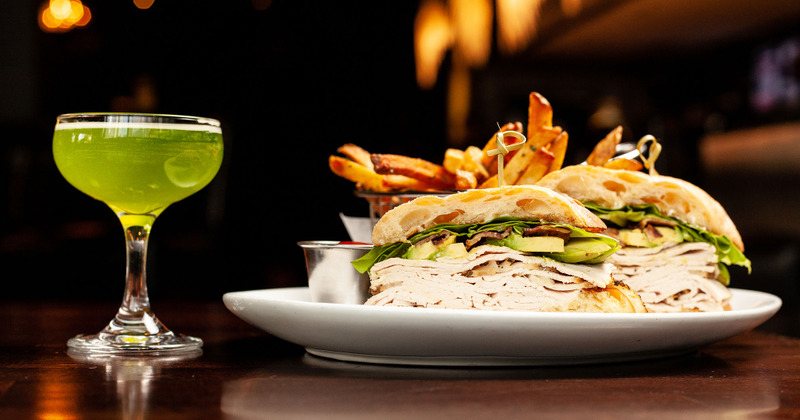 Club sandwich with fries on a plate and a glass of a green cocktail drink, side view