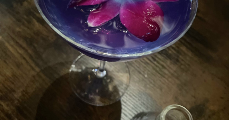 A top view of a glass of purple drink garnished with a flower