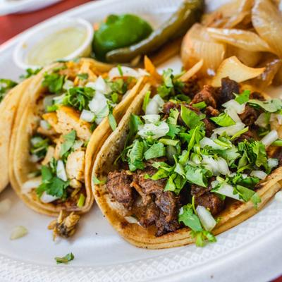 Tacos garnished with fresh diced onions and chopped cilantro, close-up.