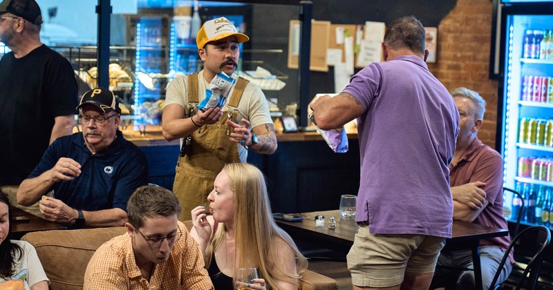 Group of people socializing in a cafe, some holding snacks and drinks, enjoying a casual atmosphere