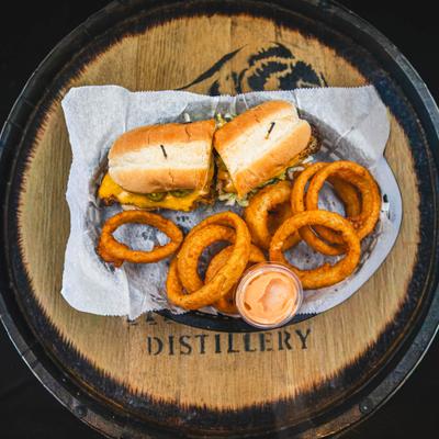 Sandwich topped with cheese and jalapeños, served with a side of onion rings and a dipping sauce.
