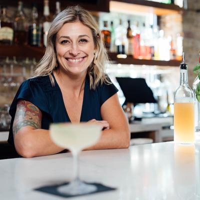 Bartender standing behind a bar and smiling, coupe glass out of focus