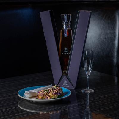 A bottle of extra-aged tequila beside a plate of food and an empty flute glass.