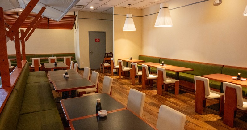 Restaurant interior with wooden tables, green booth seating, and white chairs under pendant lights