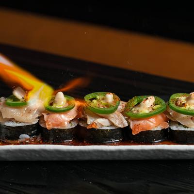 Sushi rolls on a plate being flame-seared by a torch.