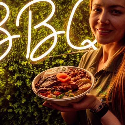 Staff member holding Top Sirloin Bowl in front of greenery neon lights signage wall