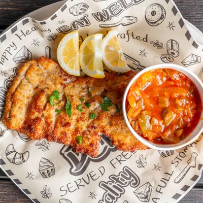 Schnitzel served with lemon wedges and a side of red sauce or dip.