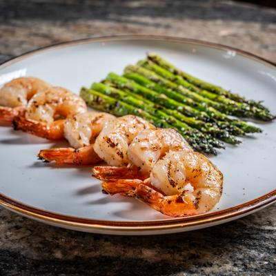 A white plate with Grilled Shrimp and Asparagus, rests on a marble surface.
