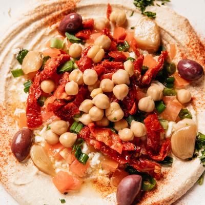 Hummus topped with chickpeas, tomatoes, olives, roasted garlic and green onion