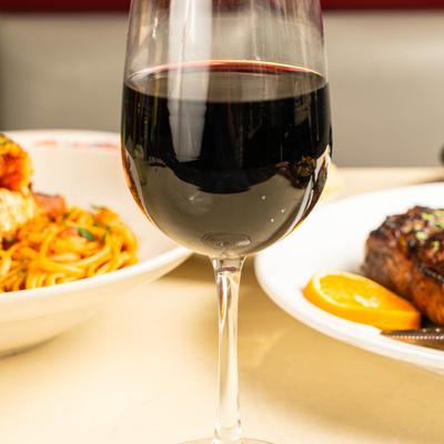 A glass or red wine sits on a white table with food.