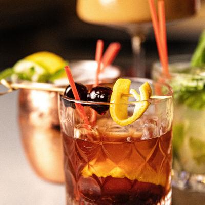 Old Fashioned garnished with lemon peel and cherries, close-up.