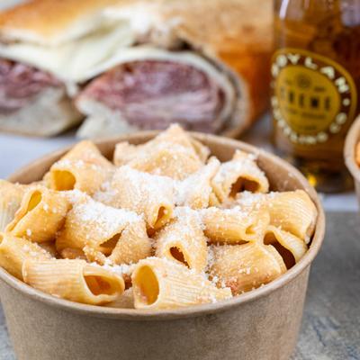 Rigatoni pasta with grated cheese served in a paper bowl.