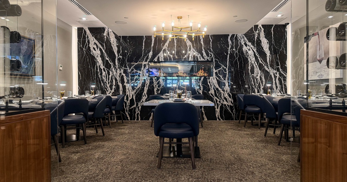 Elegant dining area with black marble walls, blue chairs, and a modern chandelier