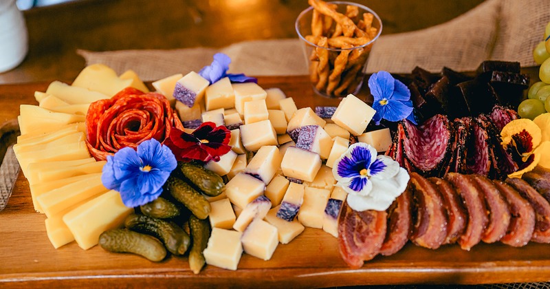 Charcuterie board featuring variety of cheeses, meats, edible flowers, and pickles