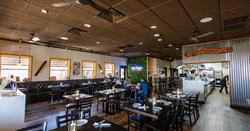 A modern restaurant interior featuring wooden tables set with plates and napkins