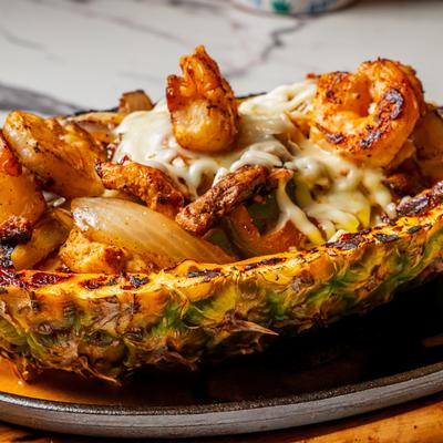 Grilled shrimp, steak, and chicken served in a carved pineapple with melted cheese.