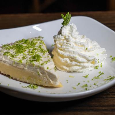 Key lime pie slice with grated lime peel and whipped cream on a white plate.