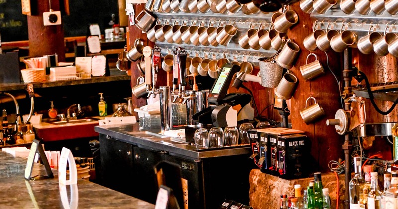 Area behind the bar with bottles, beer taps, and hung copper mugs