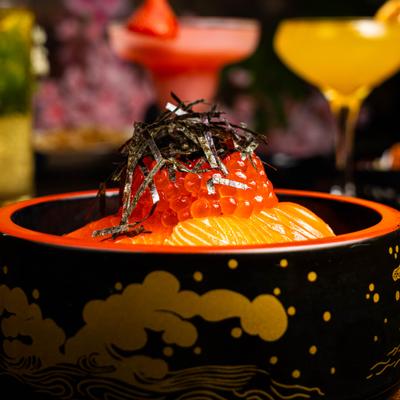 A decorative bowl with salmon sashimi served over rice, topped with cured salmon roe.