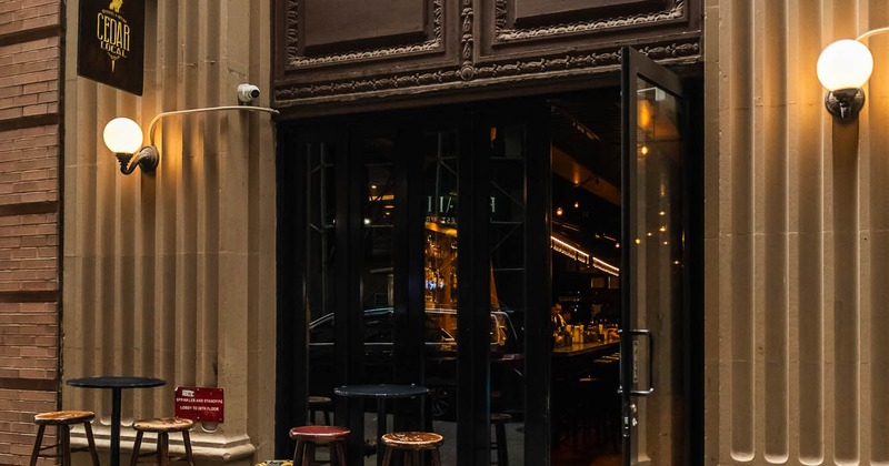 Exterior of a vintage-style bar with open glass doors, seating outside