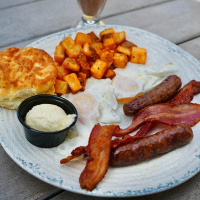 Breakfast plate with eggs, bacon, home fries, sausage links and a biscuit.
