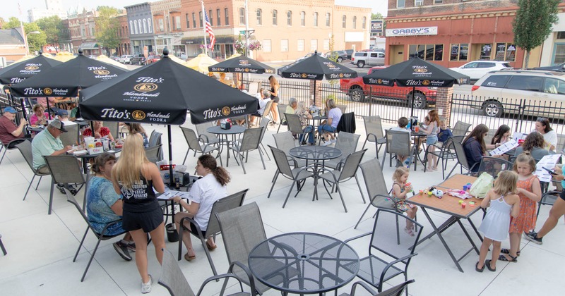 Outdoor dining area with black umbrellas and diners at tables, socializing and enjoying food