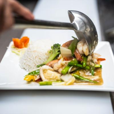 Vegetable medley with shrimp being served onto a plate next to white rice.