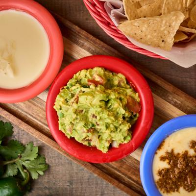 Guacamole, queso, and chips served in colorful bowls.