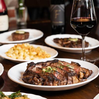 Cowboy Ribeye served on the table with glass of red wine and other dishes.