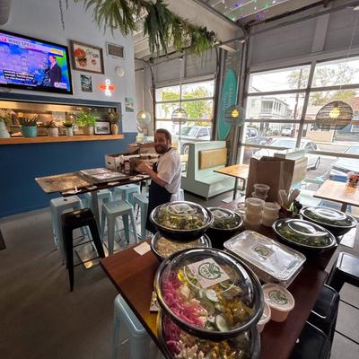 An employee in an apron stands inside a cafe, nearby, a table is filled with covered dishes.