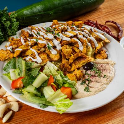 Chicken shawarma served over basmati rice with hummus, fresh salad, and sauce drizzle.
