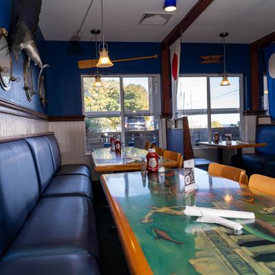 Nautical-themed restaurant interior with blue booths, ocean artwork tables, and wall decor.