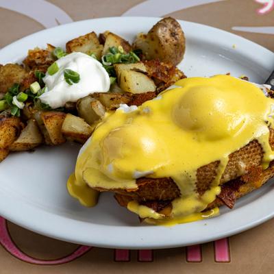 Eggs benedict alongside home fries topped with scallions and a dollop of sour cream.