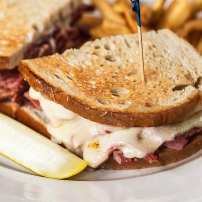 Reuben sandwich with melted cheese, corned beef, and a pickle spear.