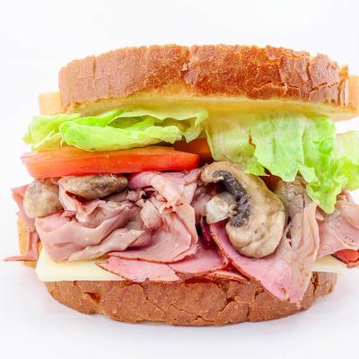 A sandwich with roast beef, mushrooms, lettuce, tomato, and cheese on rustic bread.