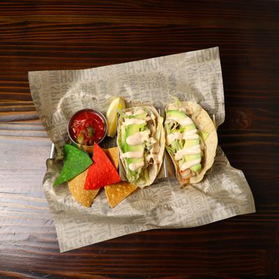 Two grilled fish tacos with corn chips.