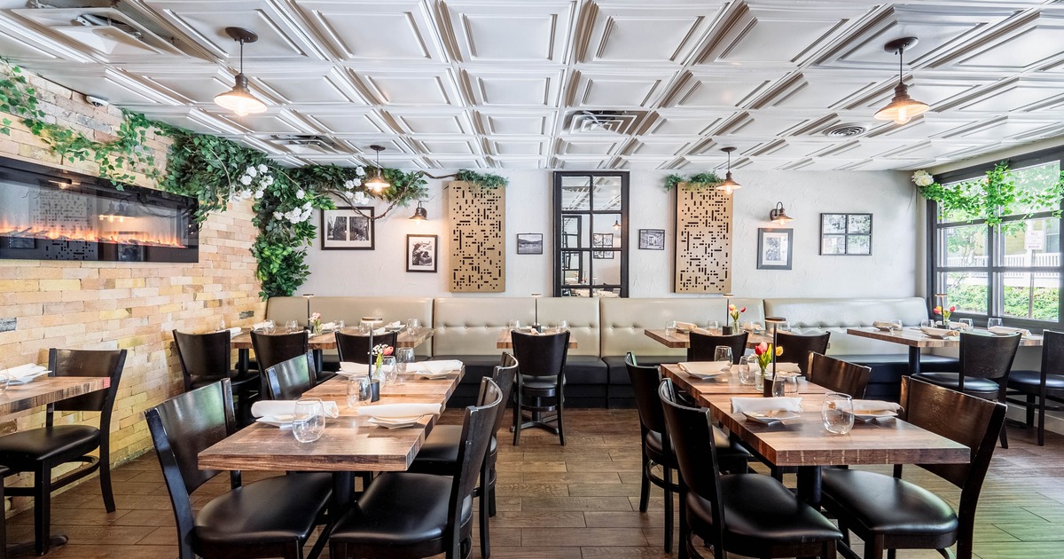 Interior with wooden tables, dark chairs, beige banquette seating, and decorative foliage