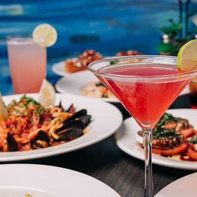 A glass of Cosmopolitan surrounded by food plates.