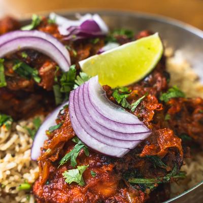 Indian spiced chicken with rice, red onion slices, cilantro, and a lime wedge.
