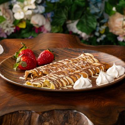 A plate of crepes drizzled with chocolate, presented with fresh strawberries and whipped cream.