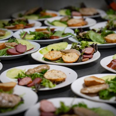 Multiple plated salads with bread and sliced meats.