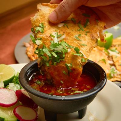 A hand dipping a slice of birria pizza into salsa.