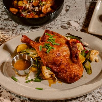 Roasted duck leg confit served with roasted vegetables and a side sauce.