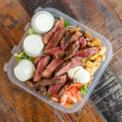 Top view of the Ribeye Steak Salad served in a plastic takeout container.