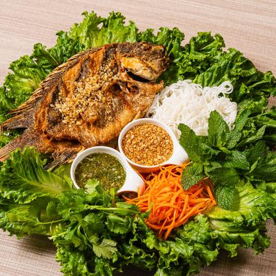 Whole fried fish with noodles, herbs, lettuce, and dipping sauces.