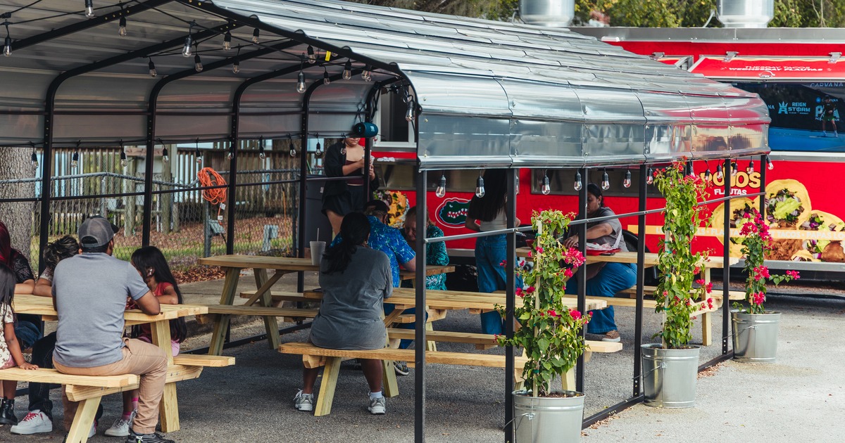 Diner area covered with an awning, tables, chairs, guests eating