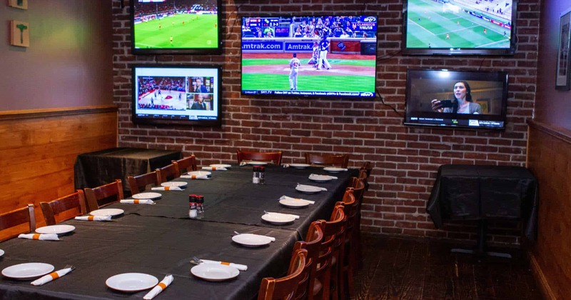 A brick-walled sports bar with TVs showing sports, A long table is set for a meal