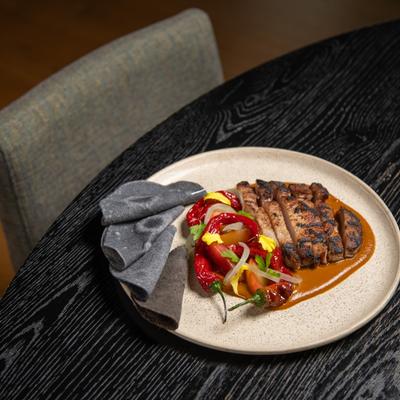 Sliced steak with roastaed peppers and tortillas on the side.
